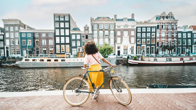 Vrouw met fiets kijkt naar panden in Amsterdam.