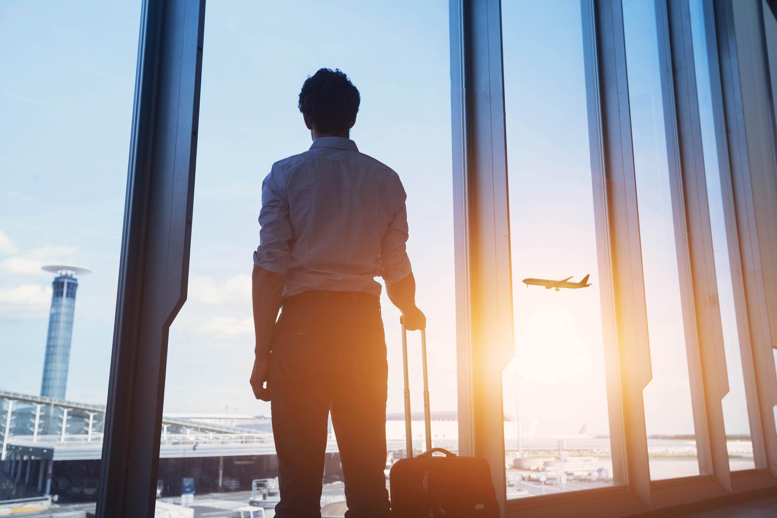 Reiziger met koffer kijkt naar een vliegtuig vanuit de terminal