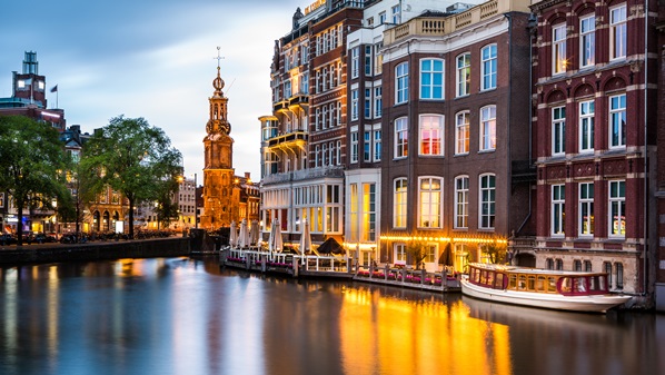 Amsterdamse gracht in de avondschemering met verlichte grachtenpanden en de Munttoren op de achtergrond