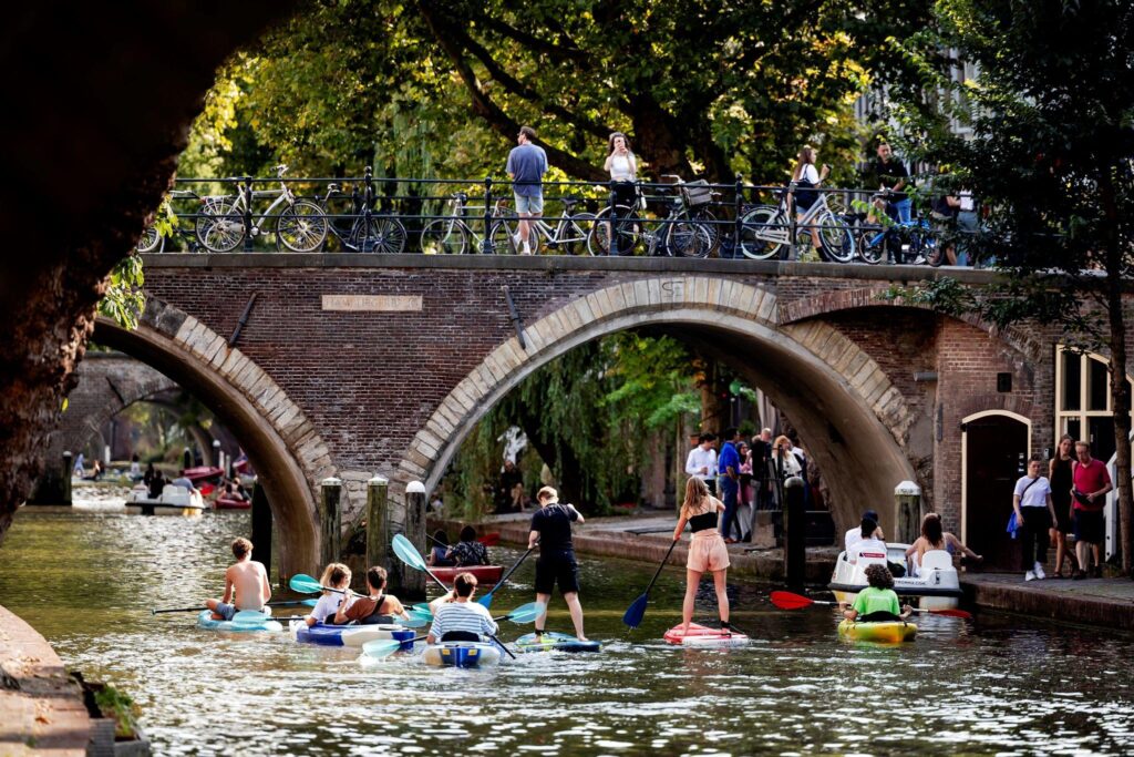 Mensen kanoën en suppen op de Utrechtse gracht bij de Hamburgerbrug op een zomerse dag